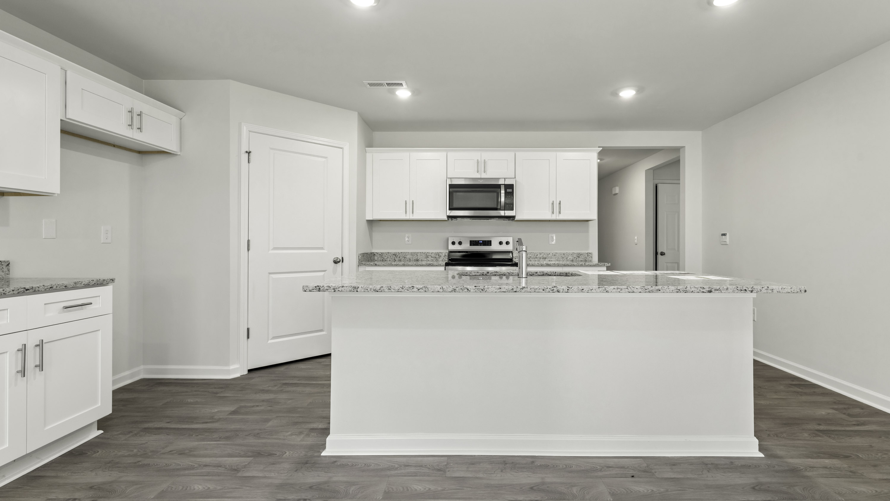 Kitchen featuring white shaker-style cabinetry, stone-surface countertops, central island, stainless steel microwave, and wood-finish flooring