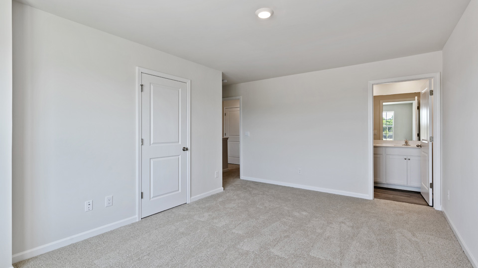 primary bedroom with two windows and carpeting, attached bath