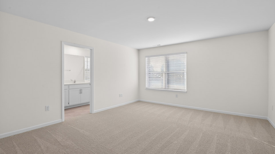 Primary bedroom with carpet floors and windows with access to the primary bathroom