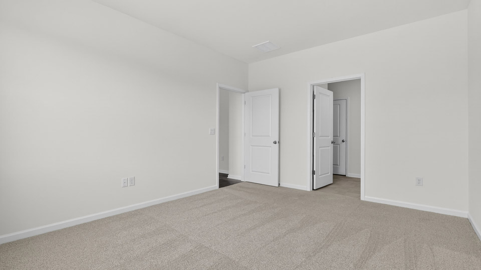 Primary bedroom with carpet floors and windows with access to the primary bathroom