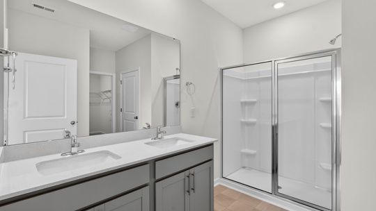 bathroom with glass door walkin shower and dual vanity with quartz countertops