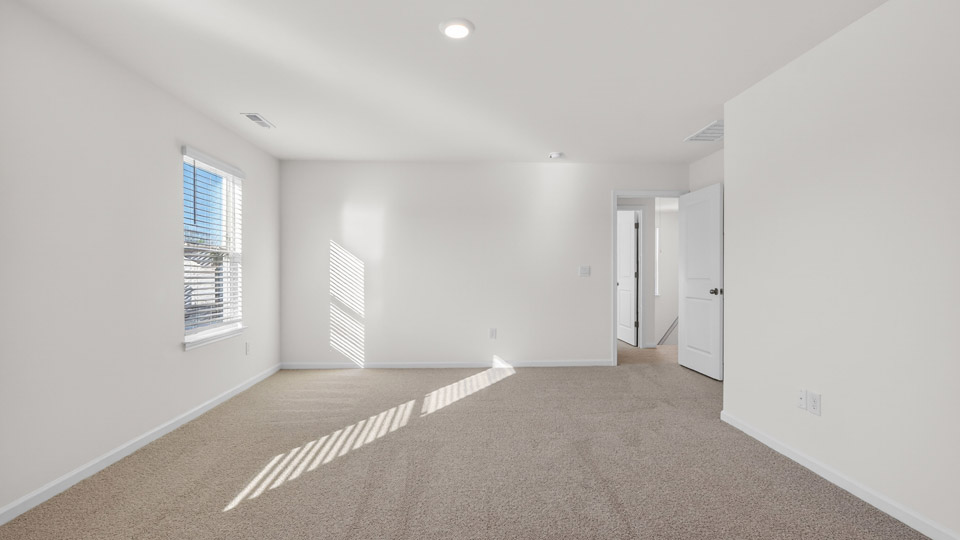 Primary bedroom with carpet floors and windows with access to the primary bathroom
