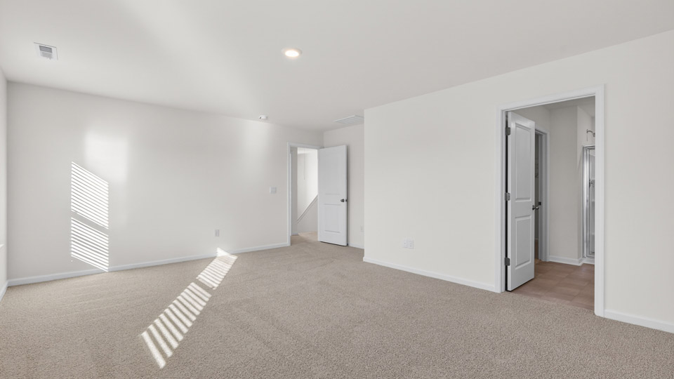 Primary bedroom with carpet floors and windows with access to the primary bathroom