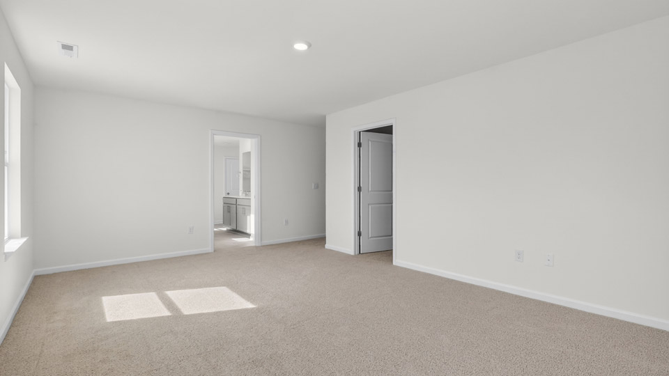 Primary bedroom with carpet floors and windows with access to the primary bathroom