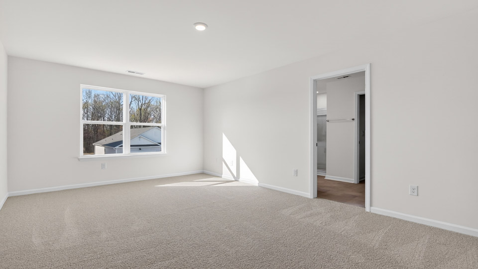 Primary bedroom with carpet floors and windows with access to the primary bathroom