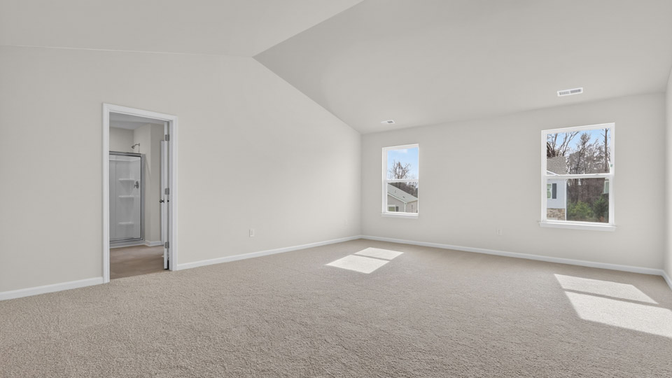 Primary bedroom with carpet floors and windows with access to the primary bathroom