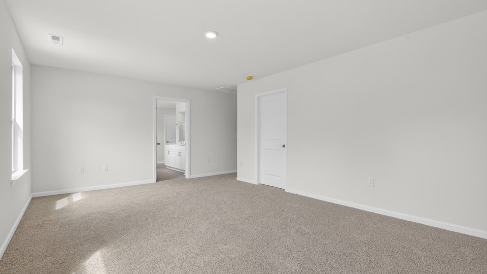 Primary bedroom with carpet floors and windows with access to the primary bathroom