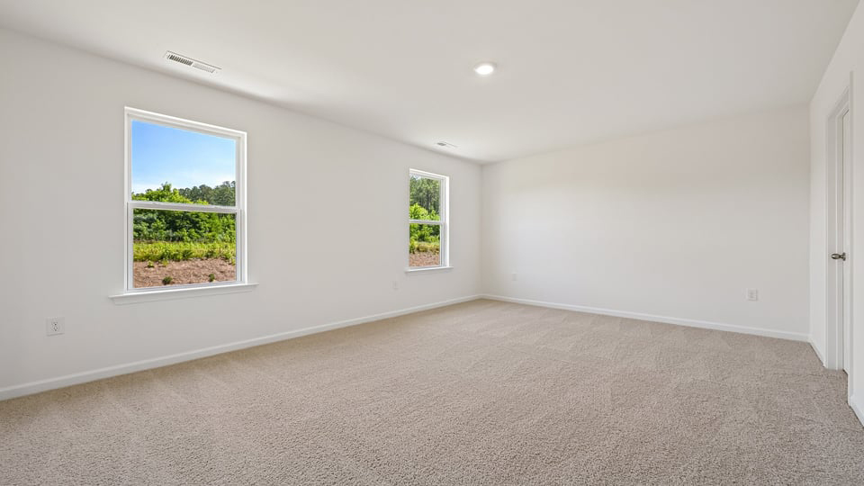 primary bedroom with two windows and carpeting, attached bath
