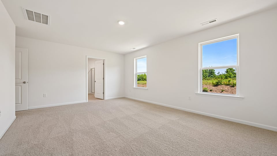 primary bedroom with two windows and carpeting, attached bath