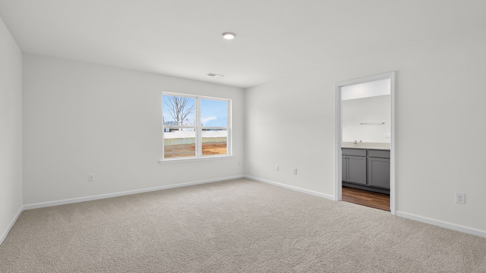 Primary bedroom with carpet floors and windows with access to the primary bathroom
