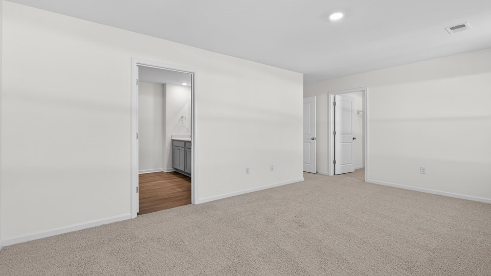 Primary bedroom with carpet floors and windows with access to the primary bathroom