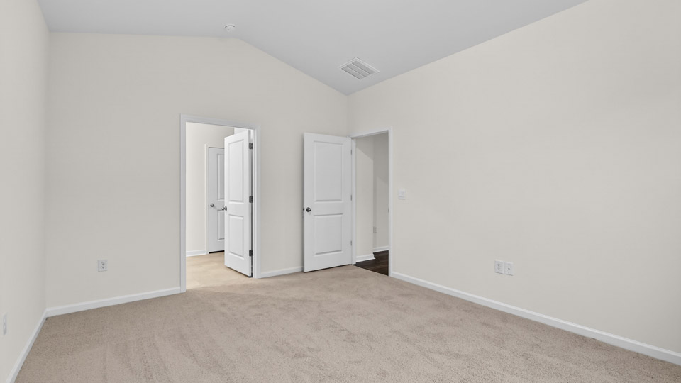 Primary bedroom with carpet floors and windows with access to the primary bathroom