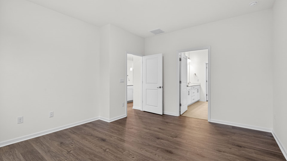 Primary bedroom with hardwood floors and windows with access to the primary bathroom