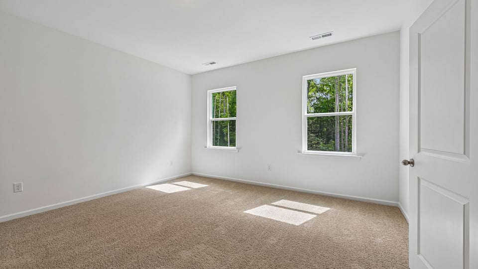 primary bedroom with two windows and carpeting, attached bath