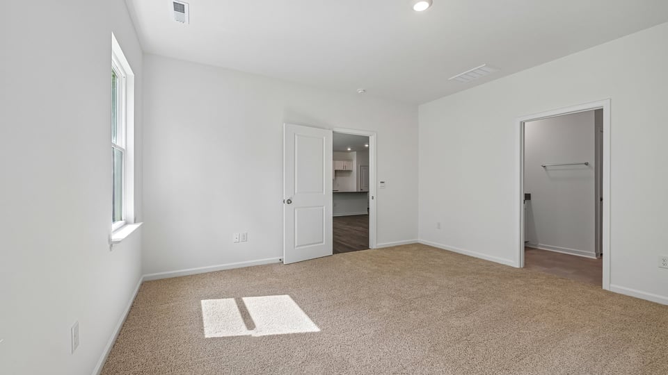 primary bedroom with two windows and carpeting, attached bath