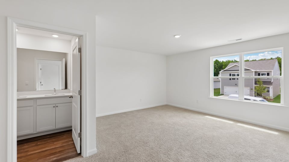 primary bedroom with two windows and carpeting, attached bath