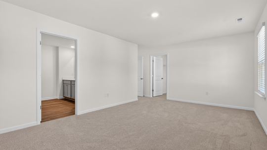 primary bedroom with two windows and carpeting, attached bath