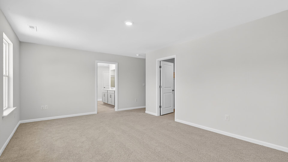 primary bedroom with two windows and carpeting, attached bath