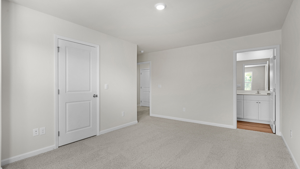 Primary bedroom with carpet floors and windows with access to the primary bathroom