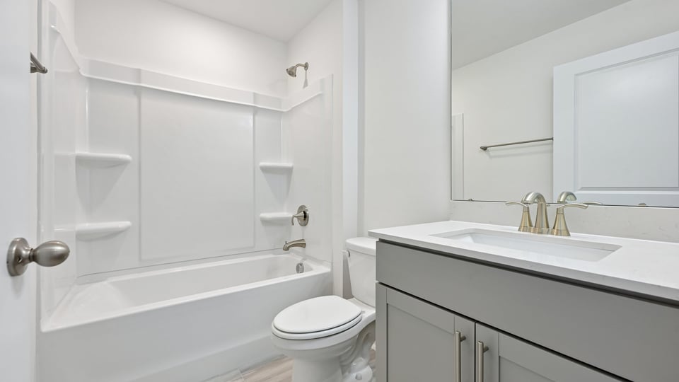bathroom with gray cabinets tub shower combo and quartz countertops