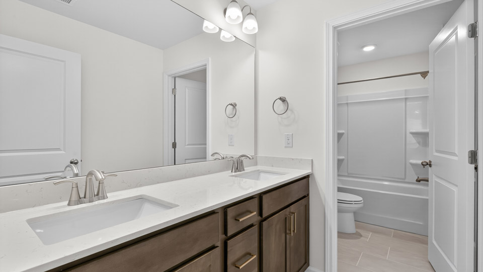 bathroom with dual vanity quartz countertops and brown cabinets