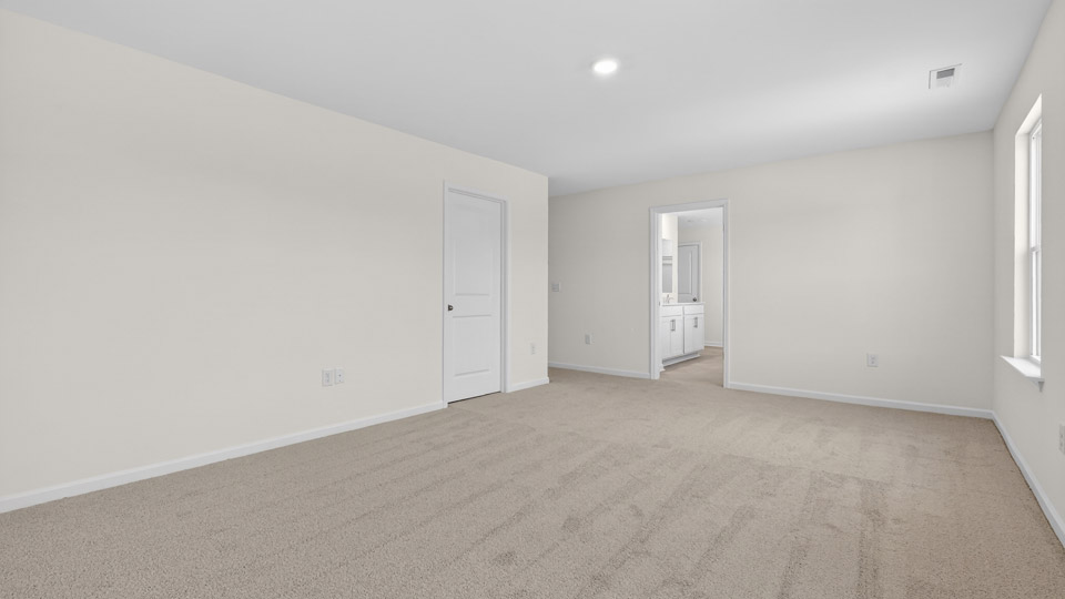 Primary bedroom with carpet floors and windows with access to the primary bathroom