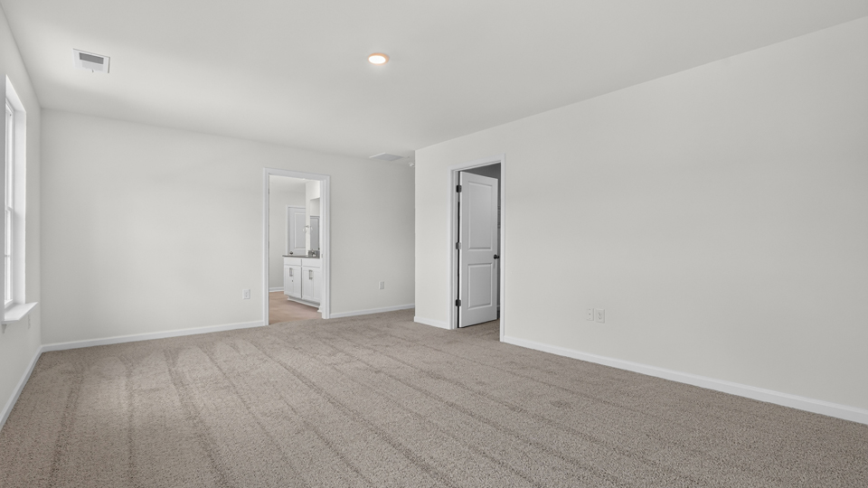 primary bedroom with two windows and carpeting, attached bath
