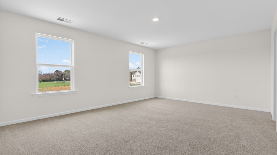 Primary bedroom with carpet floors and windows with access to the primary bathroom