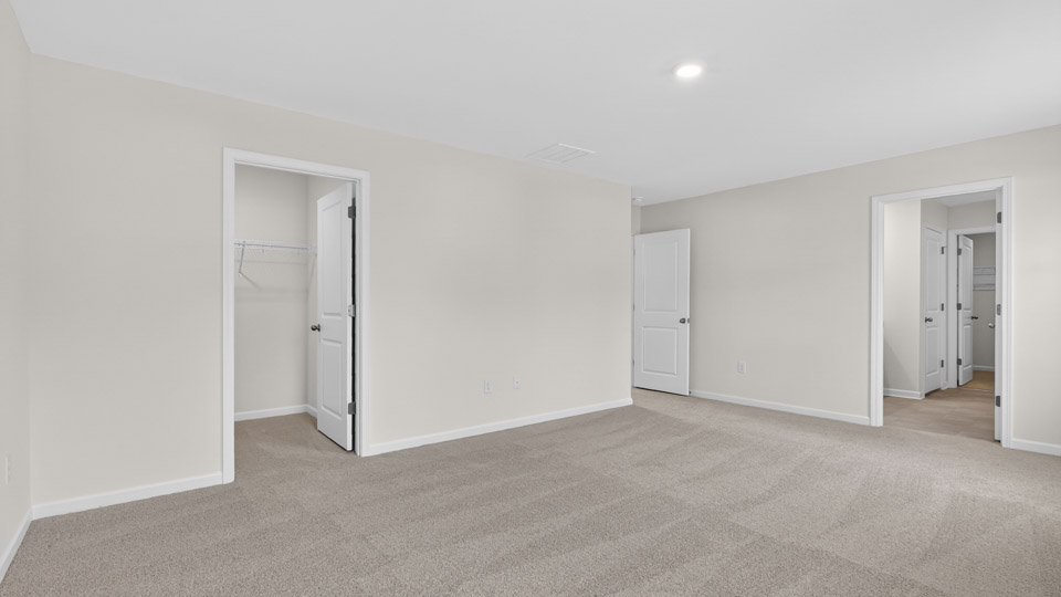 Primary bedroom with carpet floors and windows with access to the primary bathroom