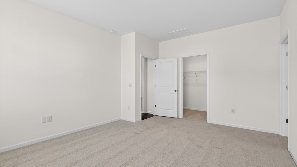 Primary bedroom with carpet floors and windows with access to the primary bathroom