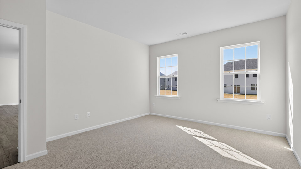 Primary bedroom with carpet floors and windows with access to the primary bathroom