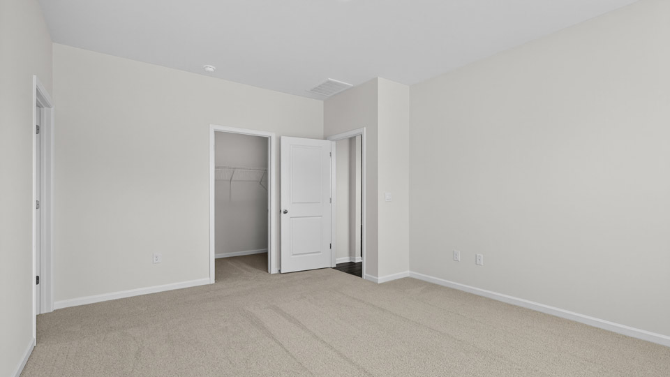 Primary bedroom with carpet floors and windows with access to the primary bathroom