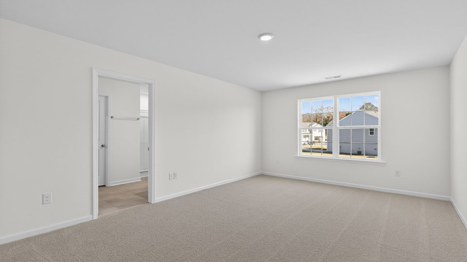 Primary bedroom with carpet floors and windows with access to the primary bathroom