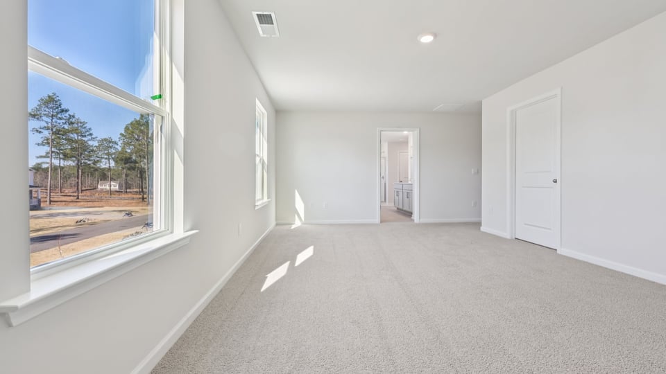 primary bedroom with two windows and carpeting, attached bath