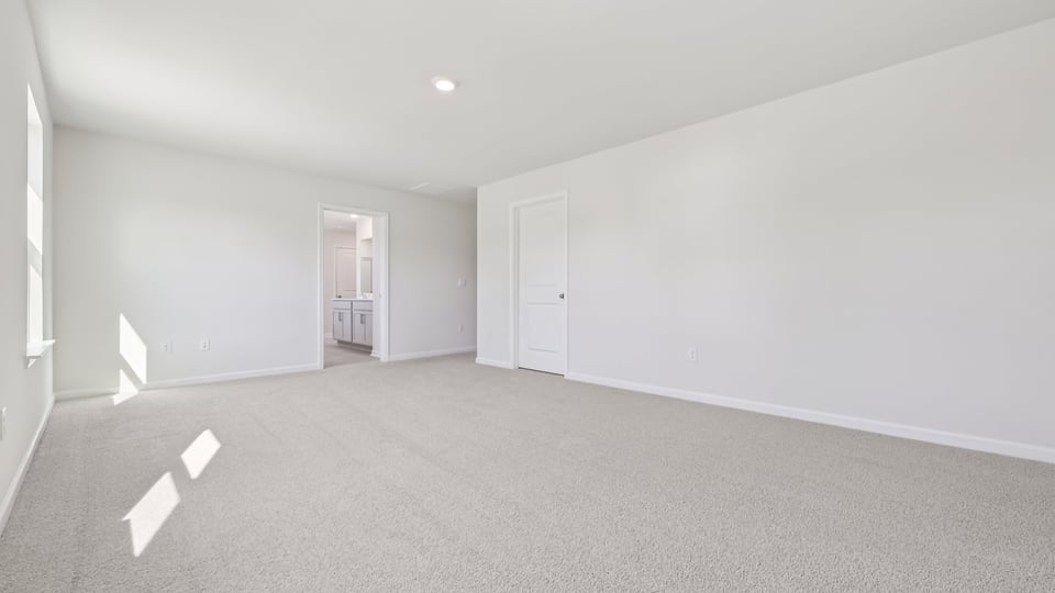primary bedroom with two windows and carpeting, attached bath