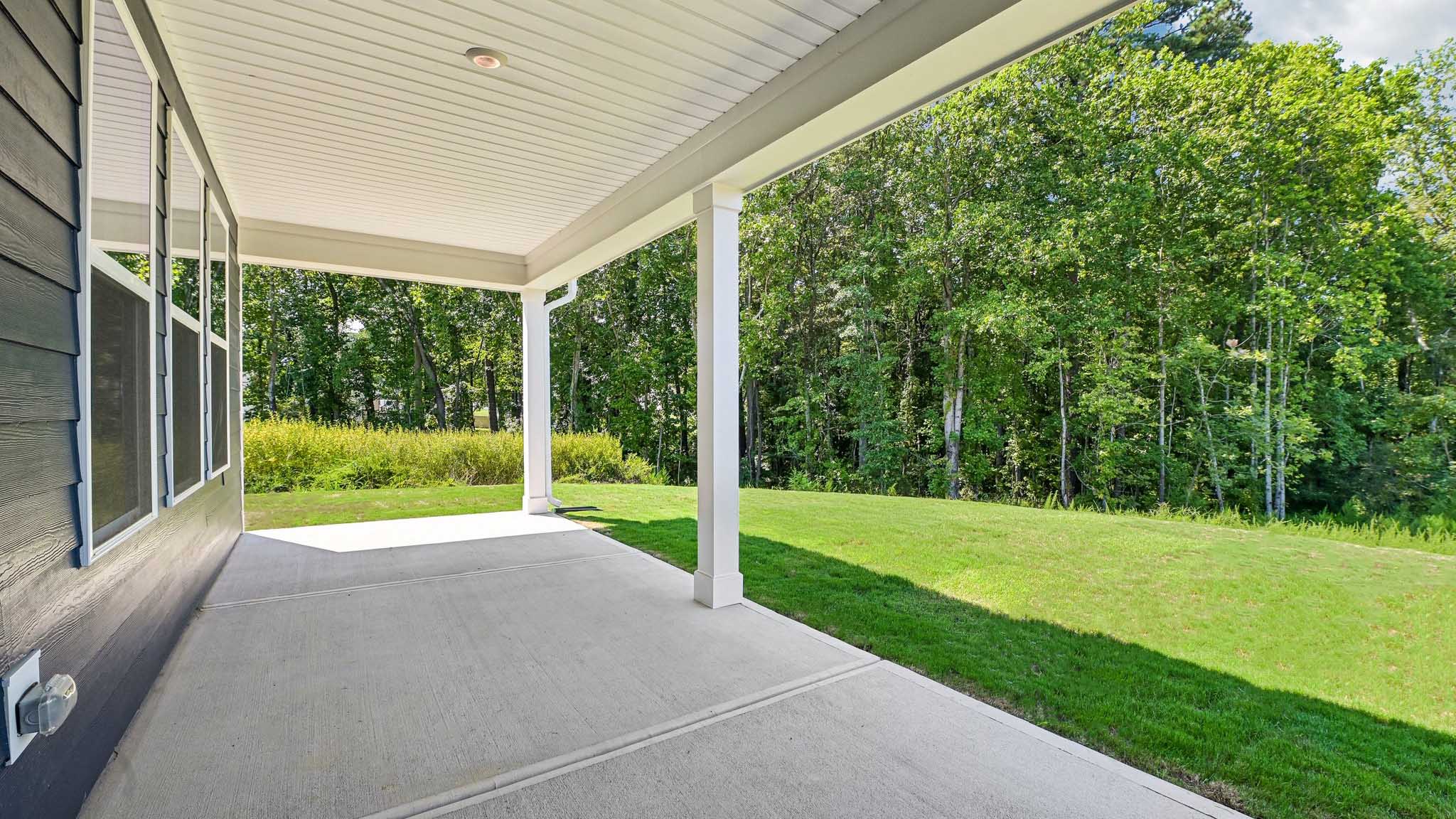 covered concrete patio and tree lined back yard