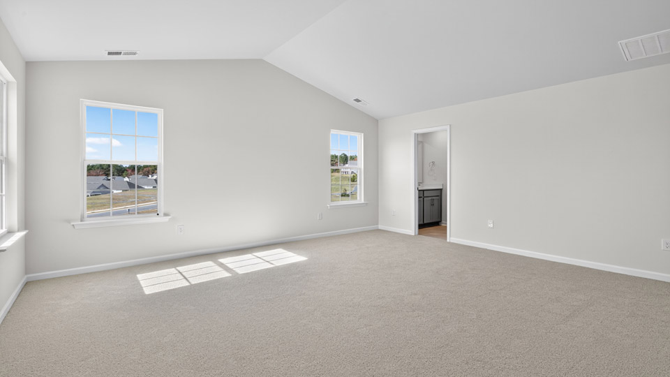 primary bedroom with two windows and carpeting, attached bath