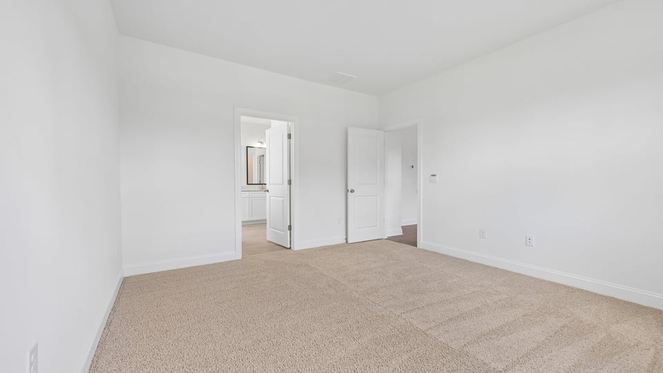 primary bedroom with two windows and carpeting, attached bath