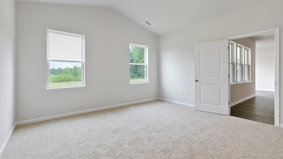 primary bedroom with two windows and carpeting, attached bath