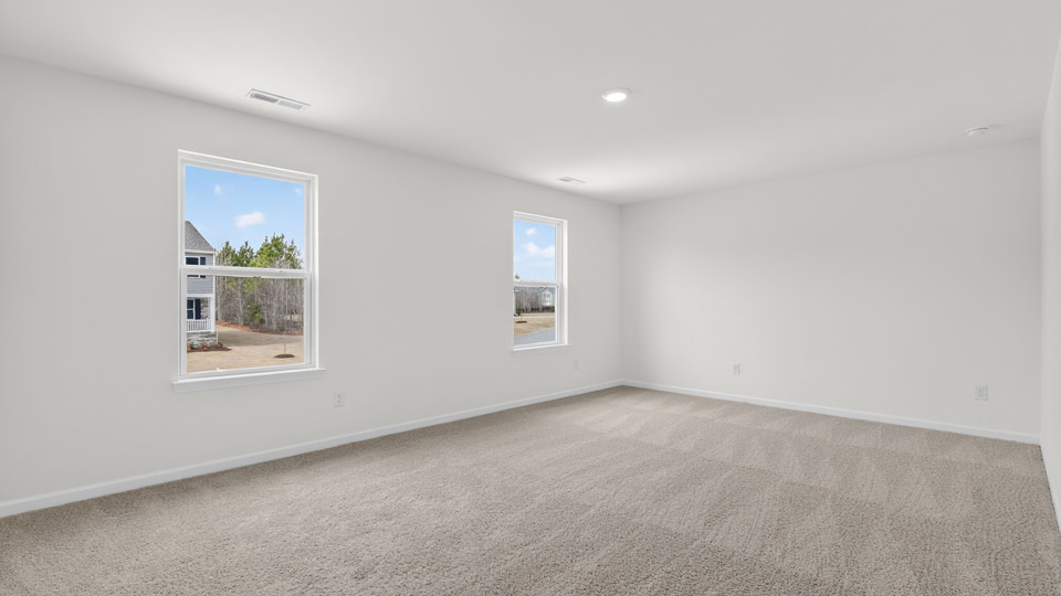 Primary bedroom with carpet floors and windows with access to the primary bathroom