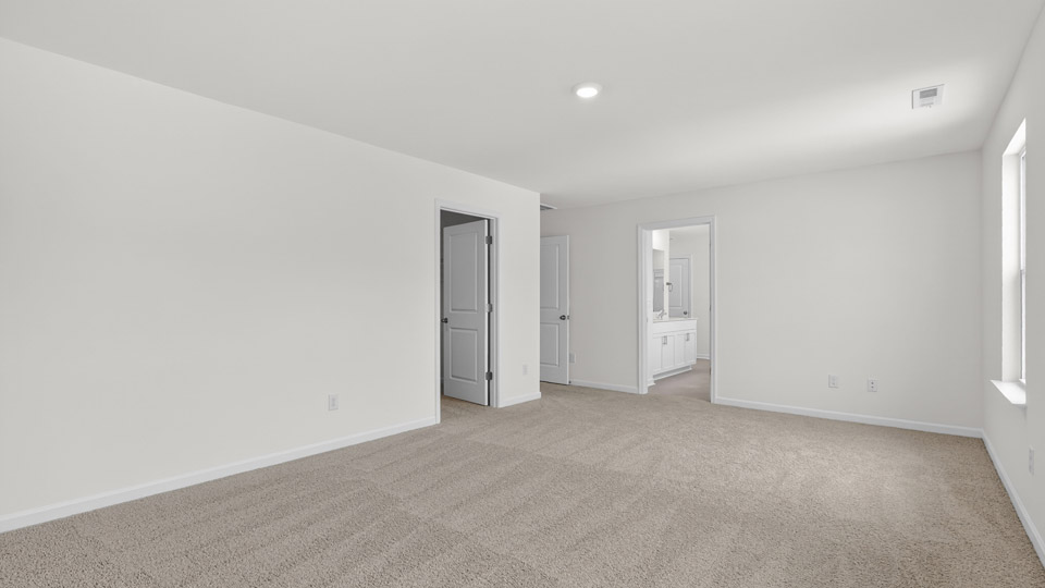 Primary bedroom with carpet floors and windows with access to the primary bathroom