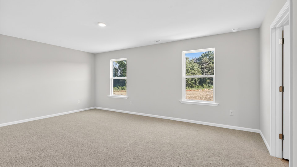 primary bedroom with two windows and carpeting, attached bath