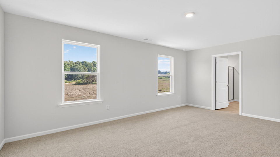 primary bedroom with two windows and carpeting, attached bath