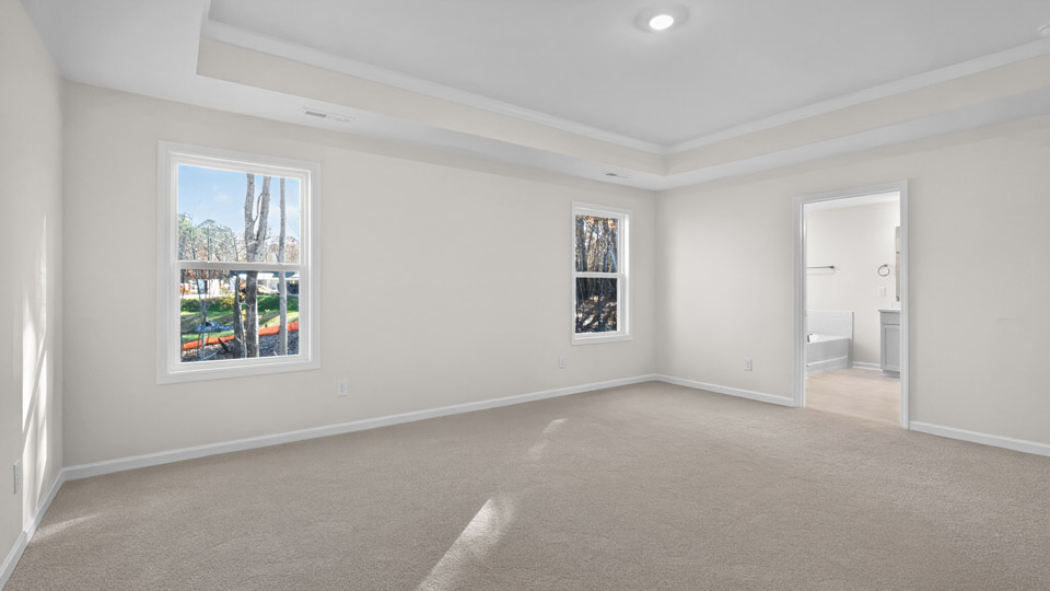 primary bedroom with two windows and carpeting, attached bath
