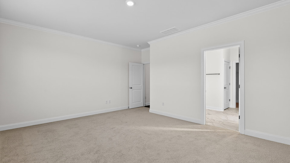 Primary bedroom with carpet floors and windows with access to the primary bathroom
