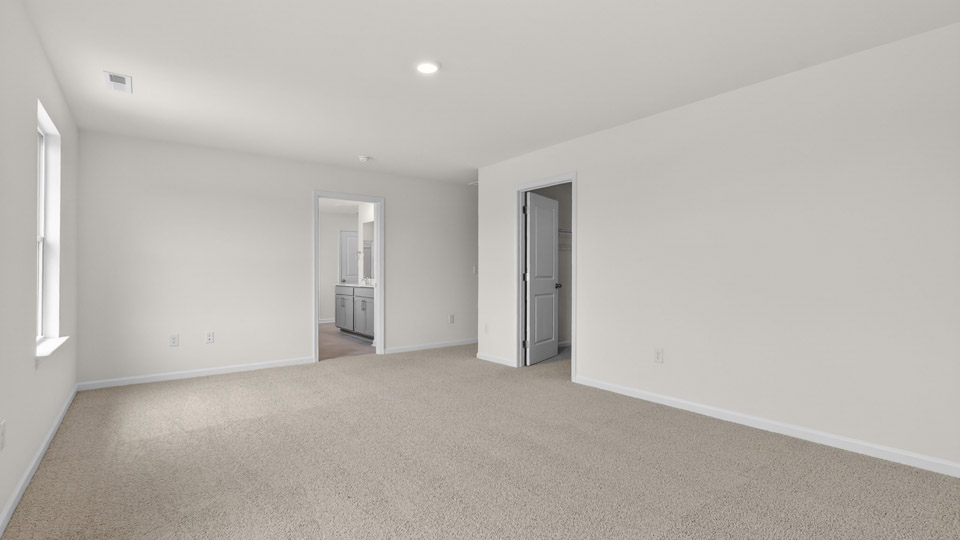 Primary bedroom with carpet floors and windows with access to the primary bathroom
