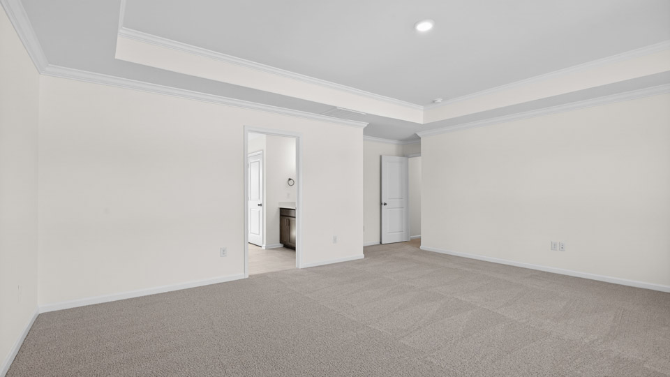 Primary bedroom with carpet floors and windows with access to the primary bathroom