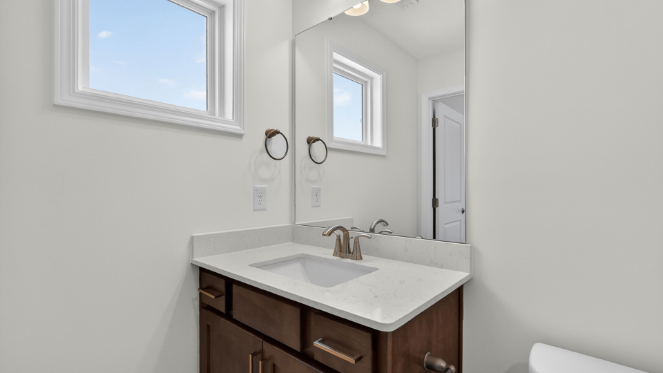 bathroom with brown cabinets window and quartz countertops