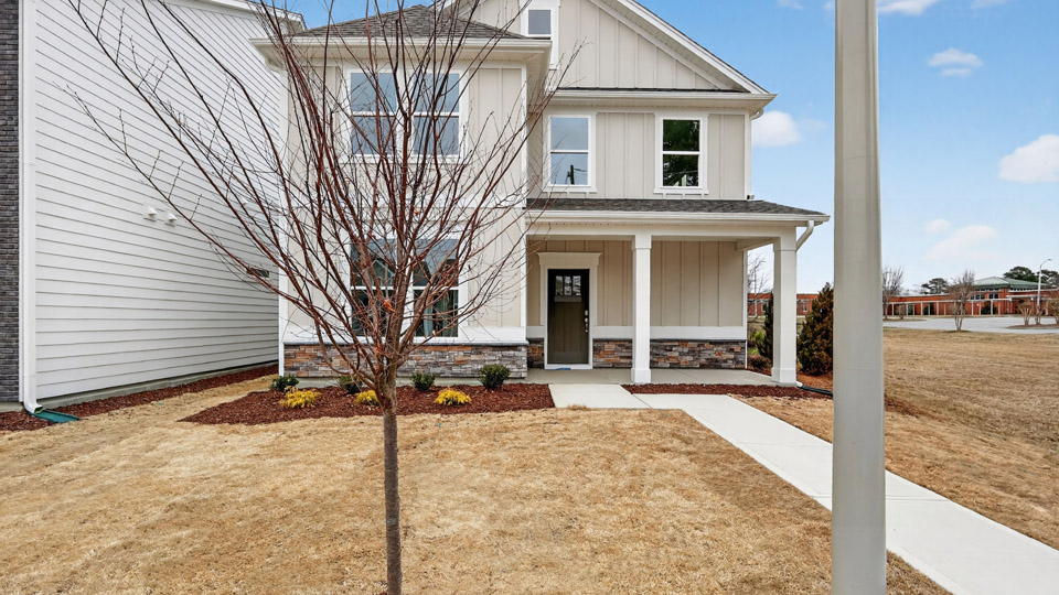 Two story home with tan colored siding with a two car garage in the back of the house