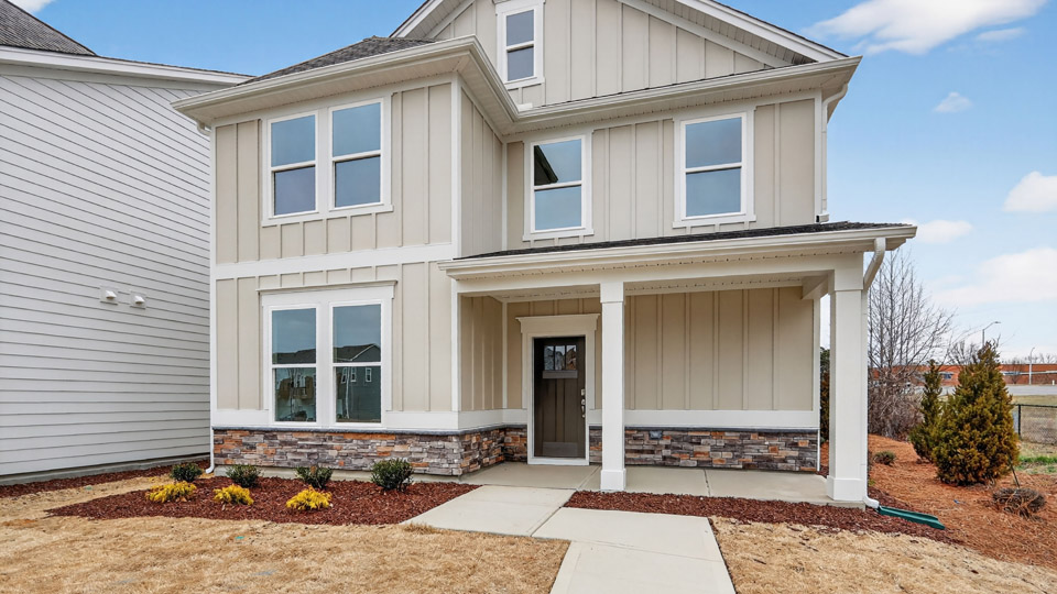 Two story home with tan colored siding with a two car garage in the back of the house